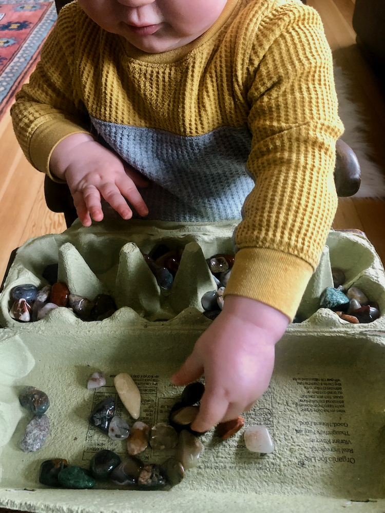 Young child placing healing crystals on the other side of an egg carton, practicing focus and mindful play.